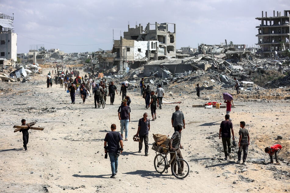 People walk along a heavily-damaged road past destroyed buildings in the center of Khan Younis in the southern Gaza Strip on October 10, 2025.