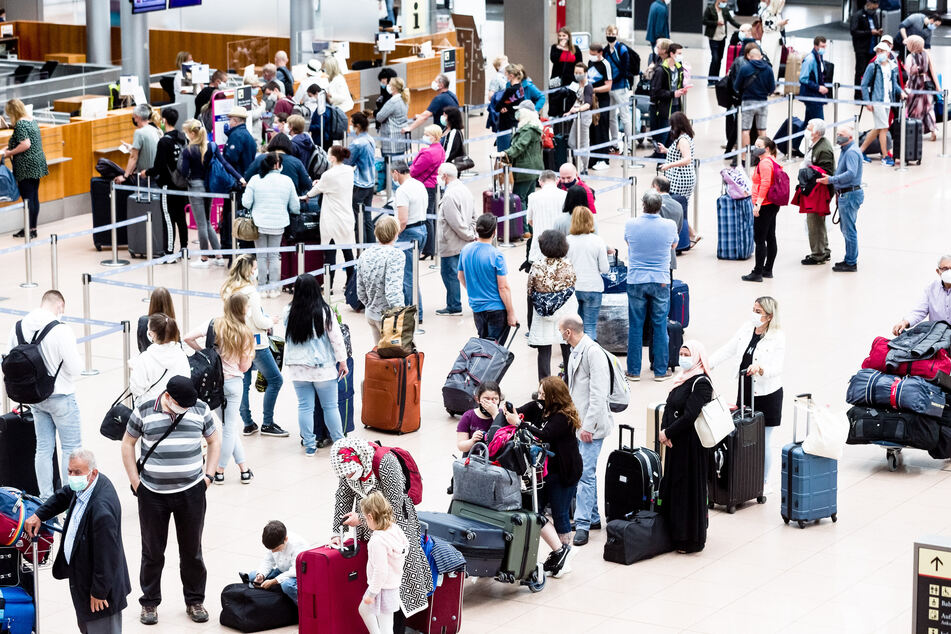 Flugpassagiere mit Mund-Nasen-Schutzmasken stehen an Check-In Schaltern des Flughafens Hamburg.