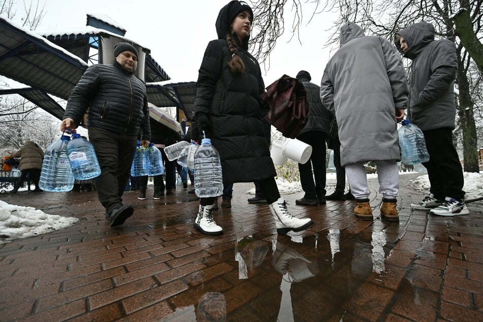 Anwohner stehen inmitten der russischen Invasion in einer Schlange vor einer Wasserpumpe in einem Park, um Plastikflaschen abzufüllen.