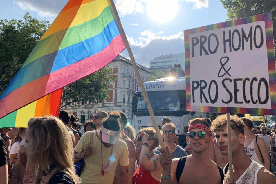 Teilnehmer der CSD-Parade am 27.07.2019 in Berlin alten ein Plakat mit der Aufschrift "Pro Homo & Pro Secco" und eine Regenbogenfahne.