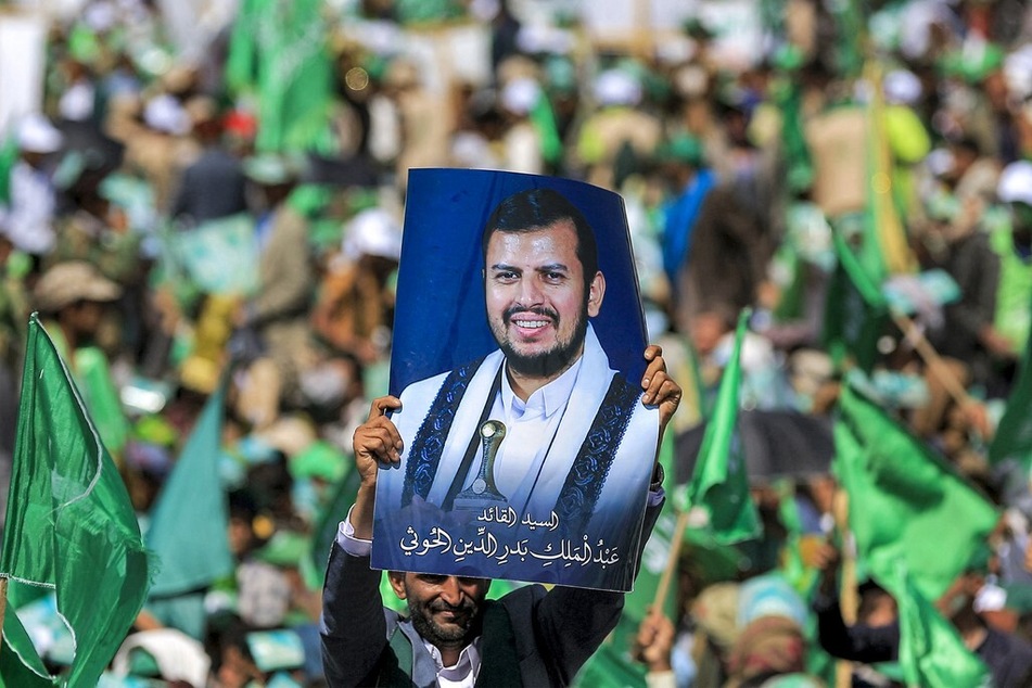 A Yemeni lifts a portrait of Huthi leader Abdel-Malek al-Huthi, who has warned the US against sending further military assets to the region.