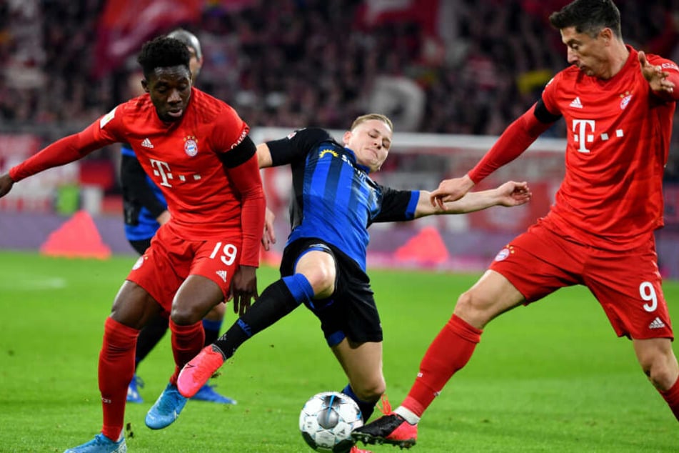Alphonso Davies (l) und Robert Lewandowski (r) vom FC Bayern München Bayern München und Kai Pröger (M) von Paderborn kämpfen um den Ball.