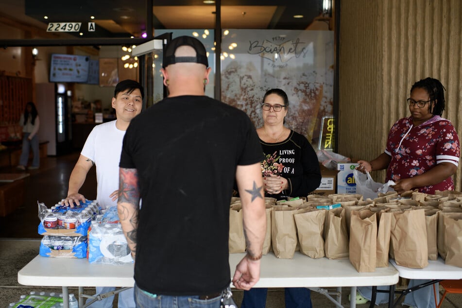 Eric Dunham approaches to receive a free lunch bag from business owner Nhan Ngo (l.) and volunteers Rashida Mize (r.) and Jennifer Unger at Petit Beignets and Tapioca Restaurant in Houston, Texas, on November 1, 2025.