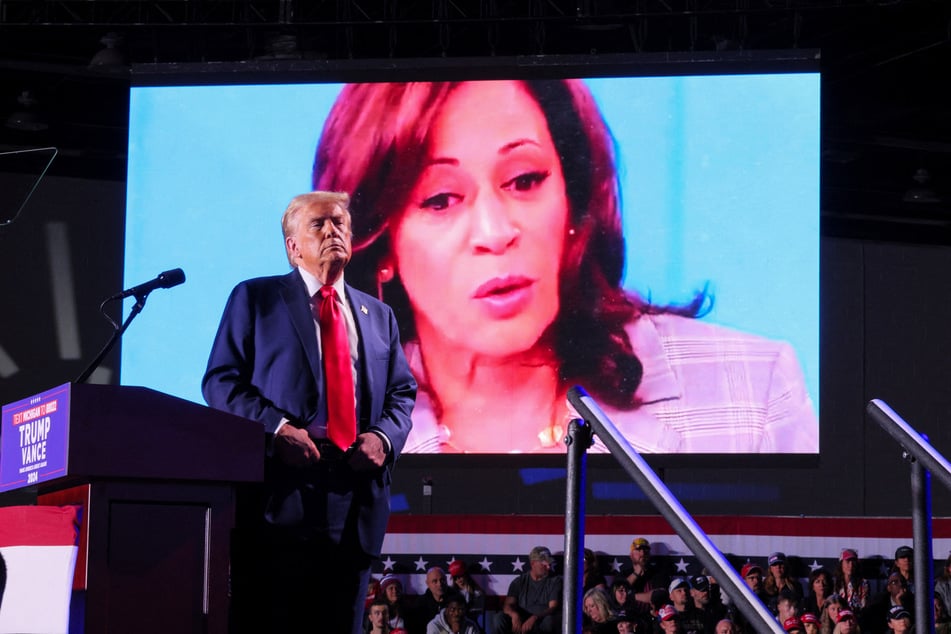 Republican presidential nominee Donald Trump looks on as Democratic Vice President Kamala Harris' face appears as a video plays on a screen during a rally at Huntington Place in Detroit, Michigan.