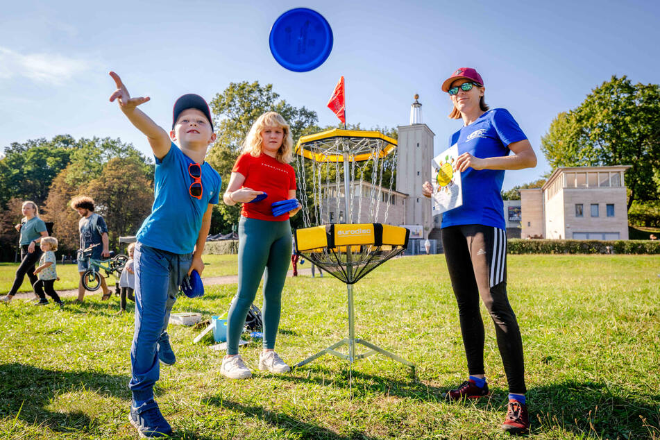 Marie-Chantal Laaser (30, r.) vom Stadtsportbund Chemnitz erklärt Oskar (6) und seine Schwester Sophia (11), wie Disc-Golf funktioniert.