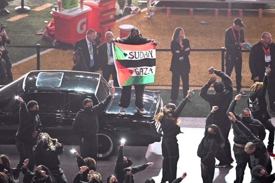 A protestor holds a Palestinian and Sudanese flag with the words "Gaza" and "Sudan" as Kendrick Lamar performs during Super Bowl LIX Chiefs vs Eagles Apple Music Halftime Show.