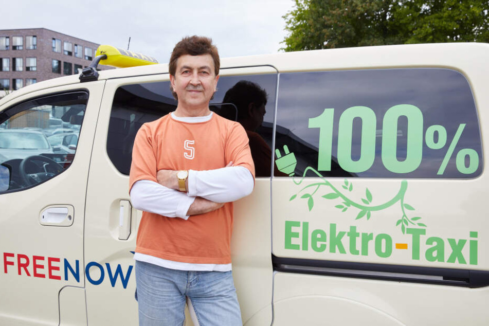 Kostyantyn Khmelevskyy, Taxifahrer, steht neben seinem Nissan e-NV 200 Evalia mit der Aufschrift: "100% Elektro-Taxi".