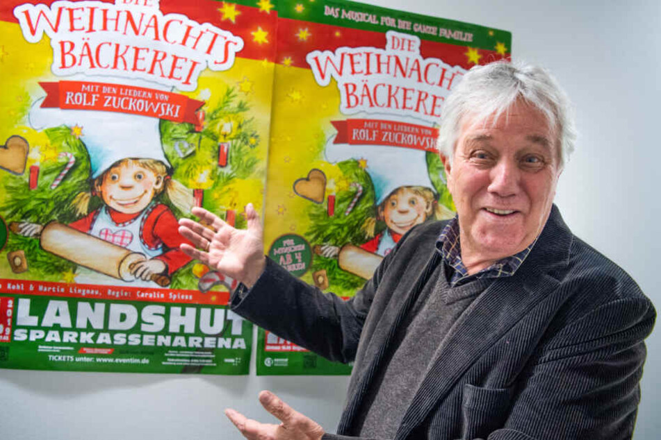 Rolf Zuckowski, Liedermacher, zeigt auf Poster seines Musicals "Die Weihnachtsbäckerei".