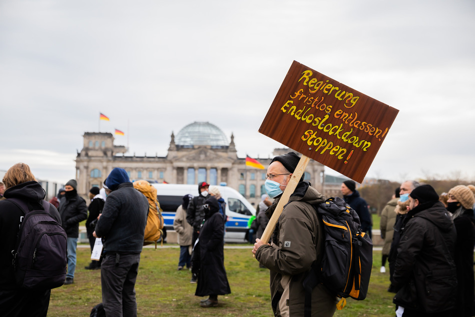 Ein Mann steht bei einer Kundgebung gegen die Corona-Maßnahmen vor dem Reichstagsgebäude. Auf dem Schild ist zu lesen „Regierung fristlos entlassen! Endloslockdown stoppen!"