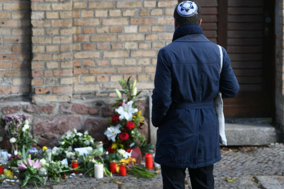 Ein Mann mit Kippa steht vor Kerzen und Blumen vor der Synagoge in Halle.