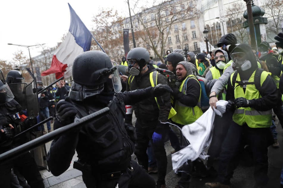 In Paris setzt ein Polizist einen Schlagstock gegen Demonstranten der "Gilets Jaunes" (Gelbwesten) ein.