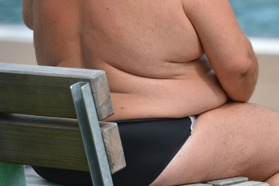 Ein übergewichtiger Mann sitzt am Strand.