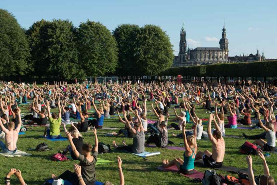 Zahlreiche Teilnehmer sitzen am 14.08.2017 in Dresden während eines Yoga-Kurses vor der Kulisse der Dresdner Altstadt auf einer Wiese.