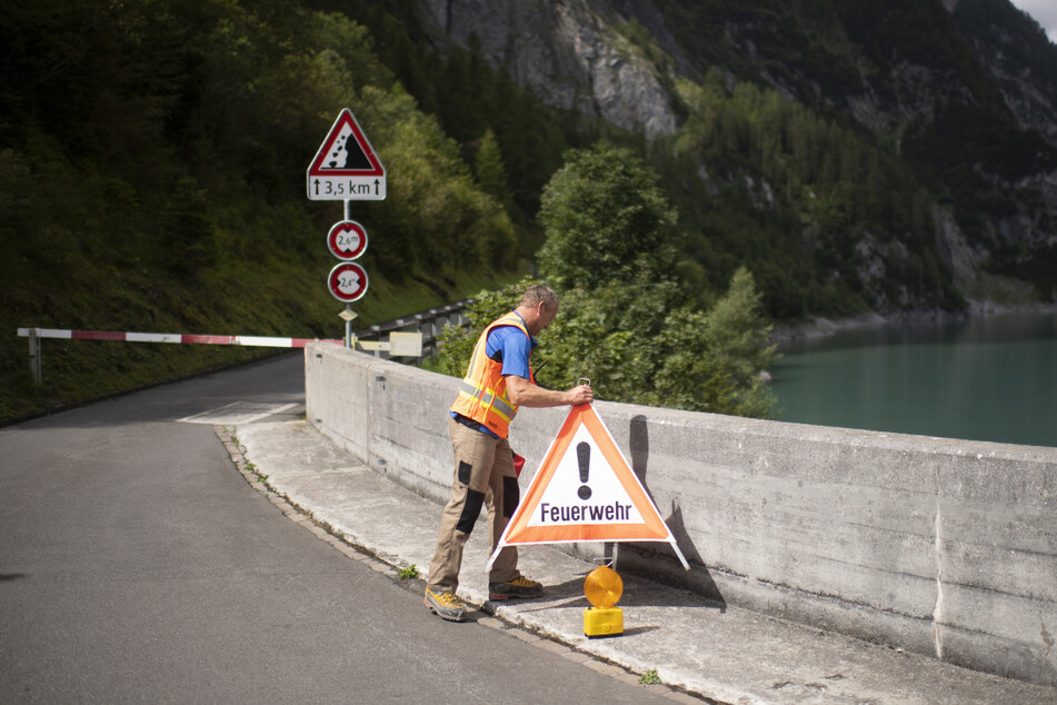 Ein Mann errichtet an der Staumauer am Gigerwaldsee eine Straßensperre für die Feuerwehr.