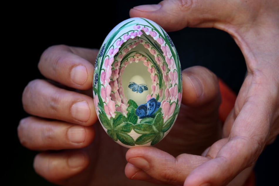 Eine Frau hält im Allgäuer Ostereier-Museum ein bemaltes Osterei in das drei weitere kleinere Eier eingefügt sind.