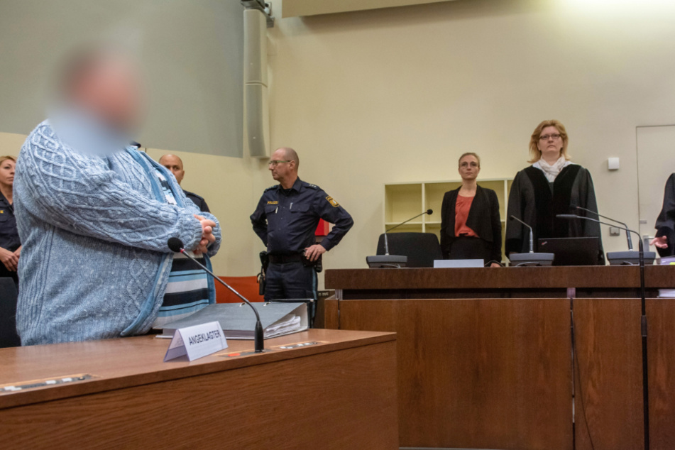 Der Angeklagte (l) steht zum Prozessauftakt an seinem Platz im Gericht.