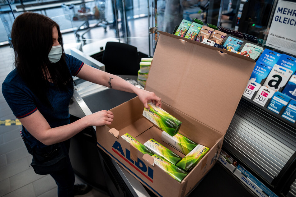 Essen: Die Aldi-Mitarbeiterin Laura Thurau packt während eines Pressetermins an einer Kasse der Aldi-Filiale Nummer 1 einen Karton mit Corona-Schnelltests aus.