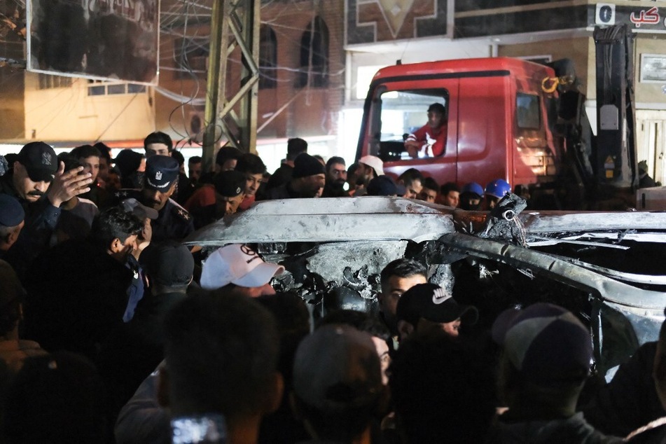 People gather around a vehicle hit by a drone strike, reportedly killing three people, in Baghdad, Iraq, on February 7, 2024.