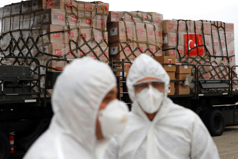 Flugbesatzungsmitglieder in Schutzkleidung stehen auf einem Rollfeld vor einer Spende von medizinischen Hilfsgütern aus der Türkei.