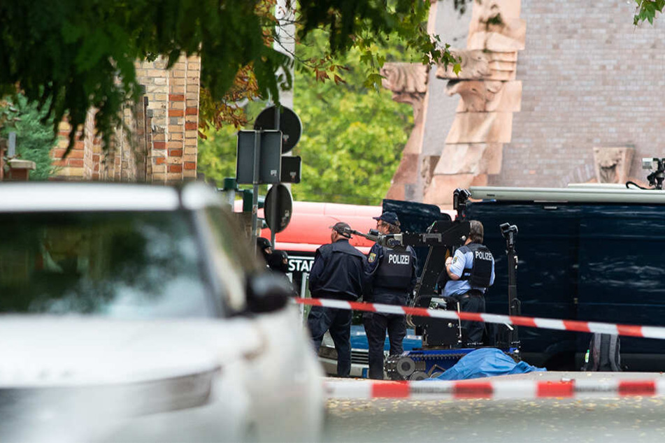 Polizisten sichern an der Mauer zur Hallenser Synagoge die Umgebung, die abgedeckte Leiche einer Frau liegt auf der Straße.