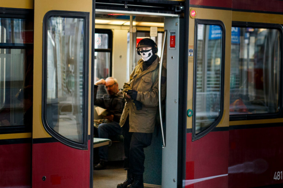 Ein Mann trägt in der S-Bahn im Bahnhof Alexanderplatz einen Munschutz auf dem Teile eine Totenkopfs abgebildet sind.
