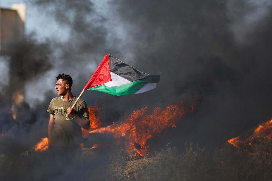 A Palestinian holds a flag as he takes part in a protest against the Israeli army raid in Jenin, along the Israel-Gaza border fence east of Gaza City.