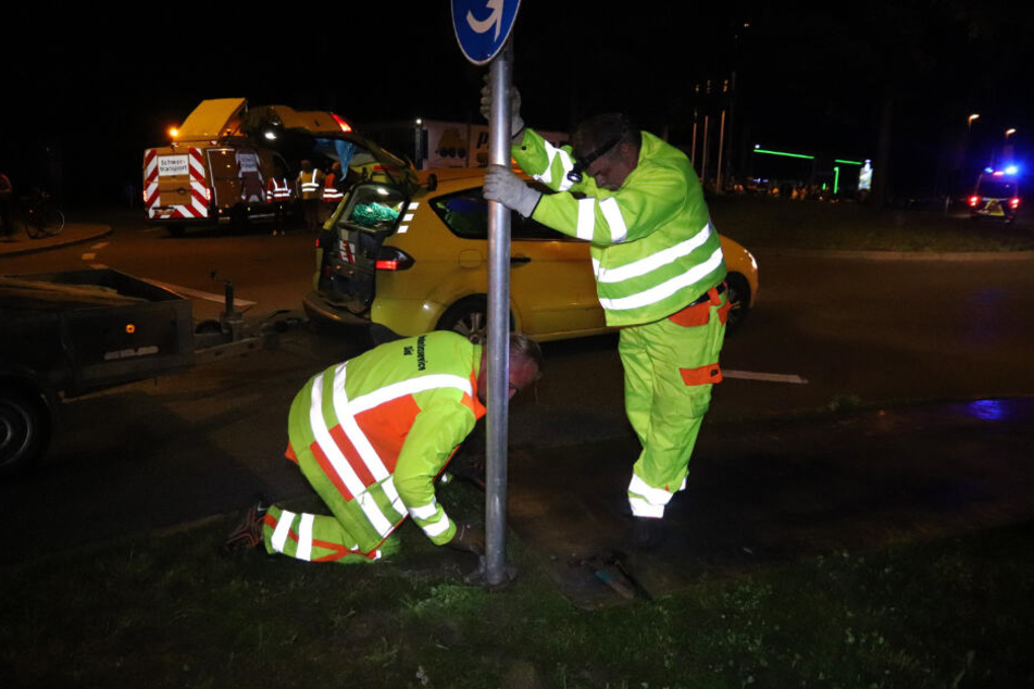 Arbeiter montieren an einer Straße ein Straßenschild für einen Schwertransporter ab.