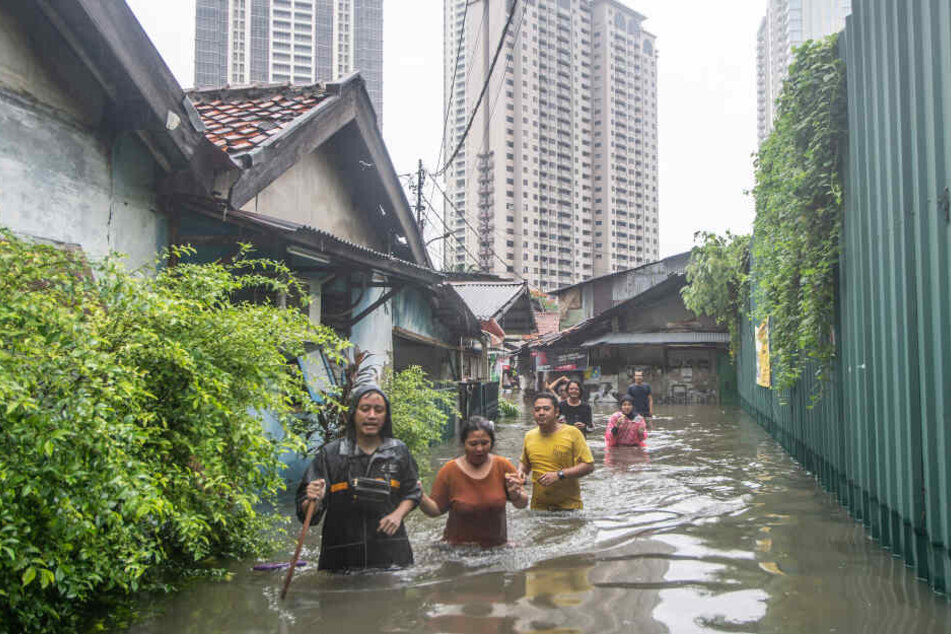 Menschen gehen auf einer vom Hochwasser überfluteten Straße.