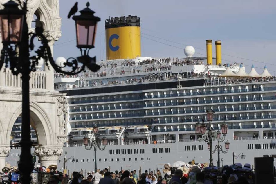Das Kreuzfahrtschiff "Costa Deliziosa" fährt am Markusplatz vorbei, auf dem zahlreiche Touristen unterwegs sind. Im Streit um Kreuzfahrtschiffe in Venedig will der Bürgermeister die Unesco auffordern, die Stadt auf die Rote Liste des gefährdeten Weltkultu