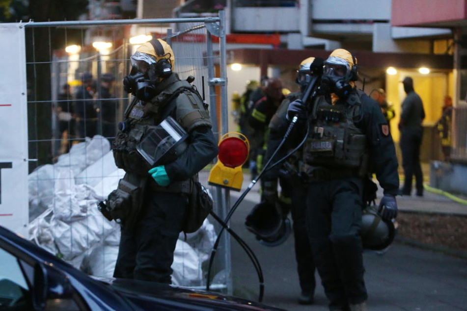 SEK Beamte mit Atemschutzmasken und Schutzanzügen verlassen das Hochhaus in Chorweiler.