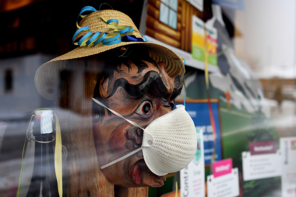 Im Schaufenster einer Apotheke trägt eine Holzlarve, die sonst Einheimische beim traditionellen Maschkera-Gehen tragen, eine FFP2-Maske. Zuhause bleiben heißt es für Hexen, Gnome und andere Faschingsgestalten.