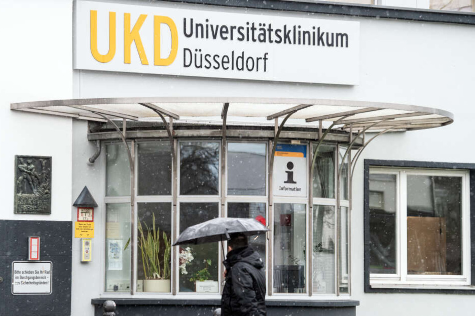 Ein Mann mit Regenschirm vor dem Gelände des Universitätsklinikums Düsseldorf.