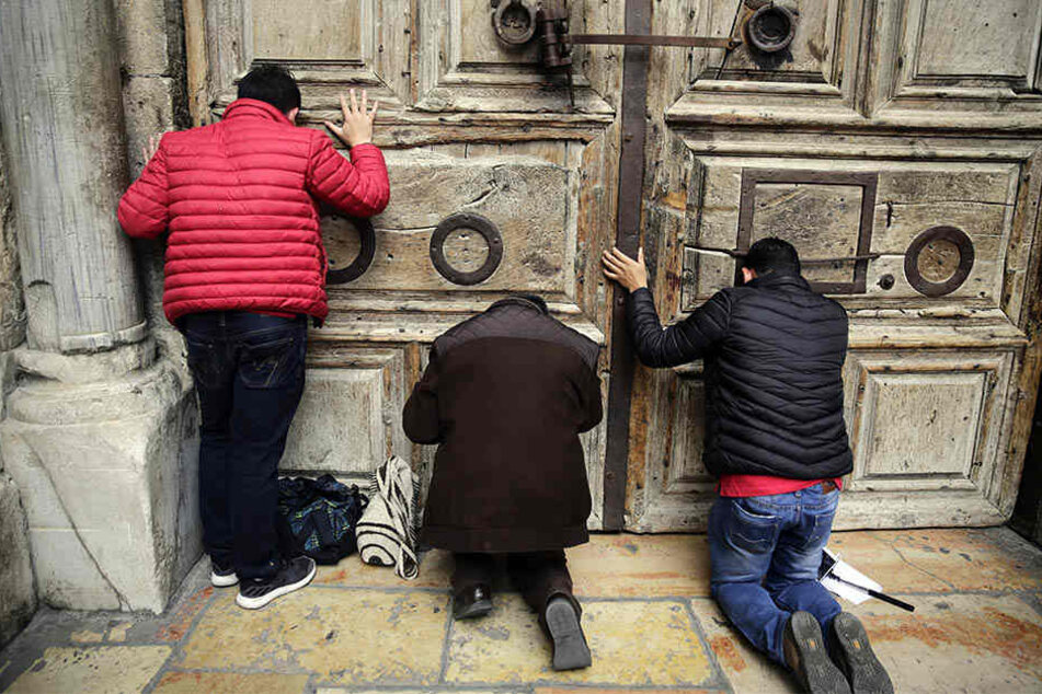 Besucher beten vor der geschlossenen Tür der Grabeskirche, der heiligsten Stätte des Christentums, in der Altstadt von Jerusalem.