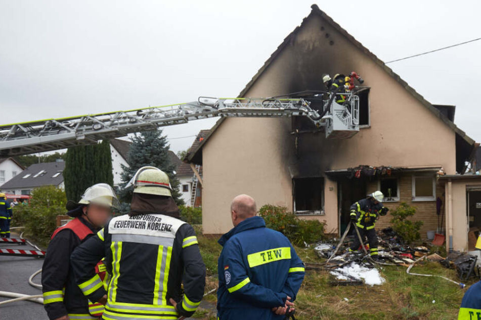Einsatzkräfte stehen vor den Ruinen des Hauses.