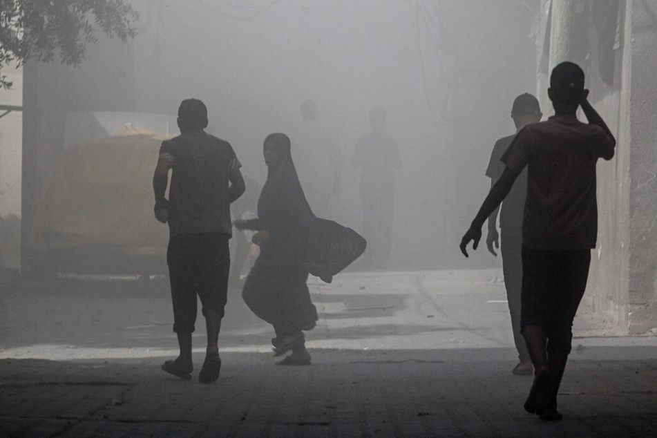 Palestinians walk through smoke and dust following an attack by the Israeli forces in the Nuseirat refugee camp, in the central Gaza Strip.