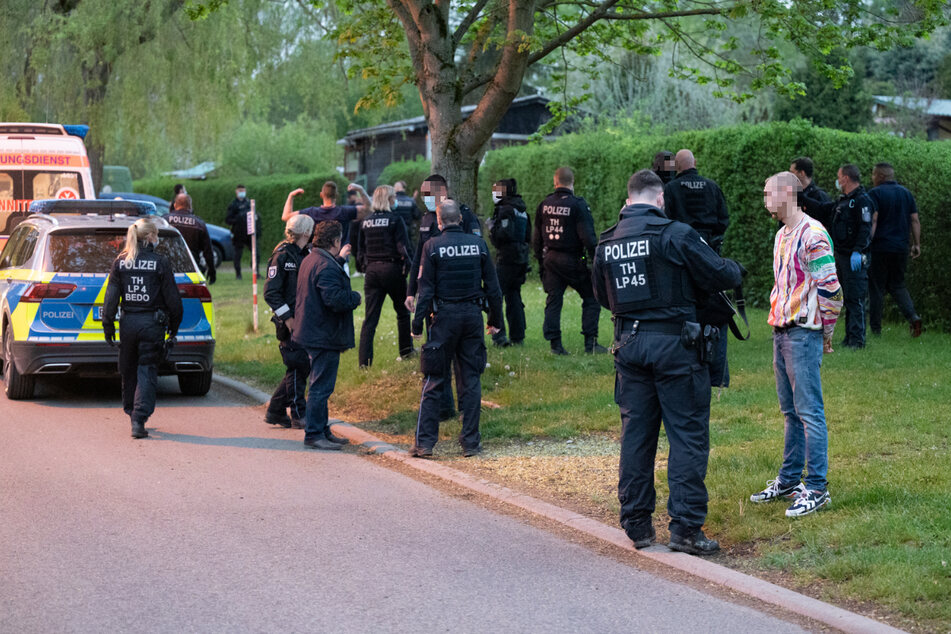 Mehrere Polizeibeamte stehen vor der Gartenanlage und befragen Personen.