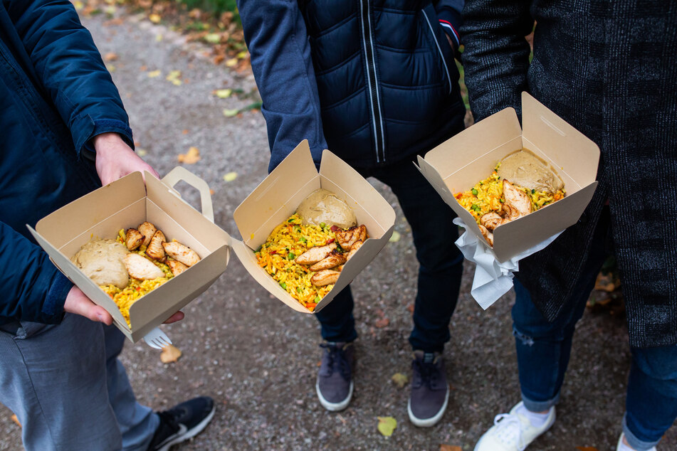 Drei Studenten stehen mit Ihrem Essen in einer Papierbox auf einer Straße.