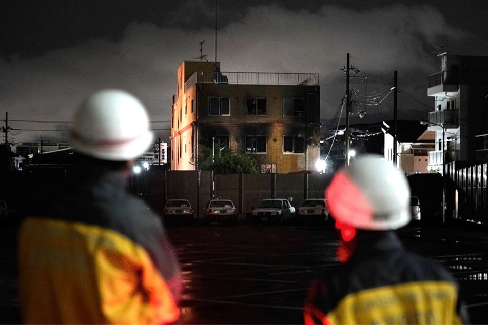 Zwei Feuerwehrleute schauen auf das ausgebrannte Gebäude nach dem Anschlag auf das berühmte Animationsstudio im japanischen Kyoto.