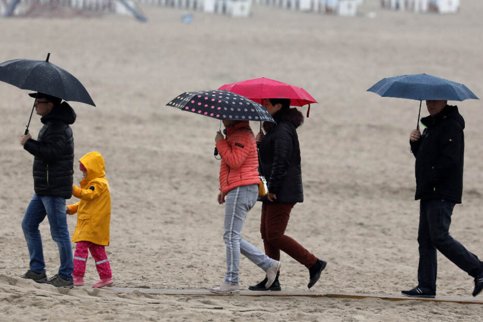 Mit Regenschirmen sind Spaziergänger an der Ostsee unterwegs.