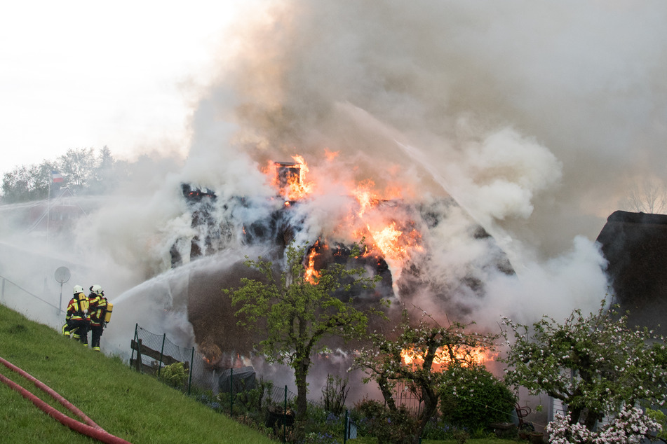 Feuerwehrleute löschen ein im Vollbrand stehendes Reetdachhaus.