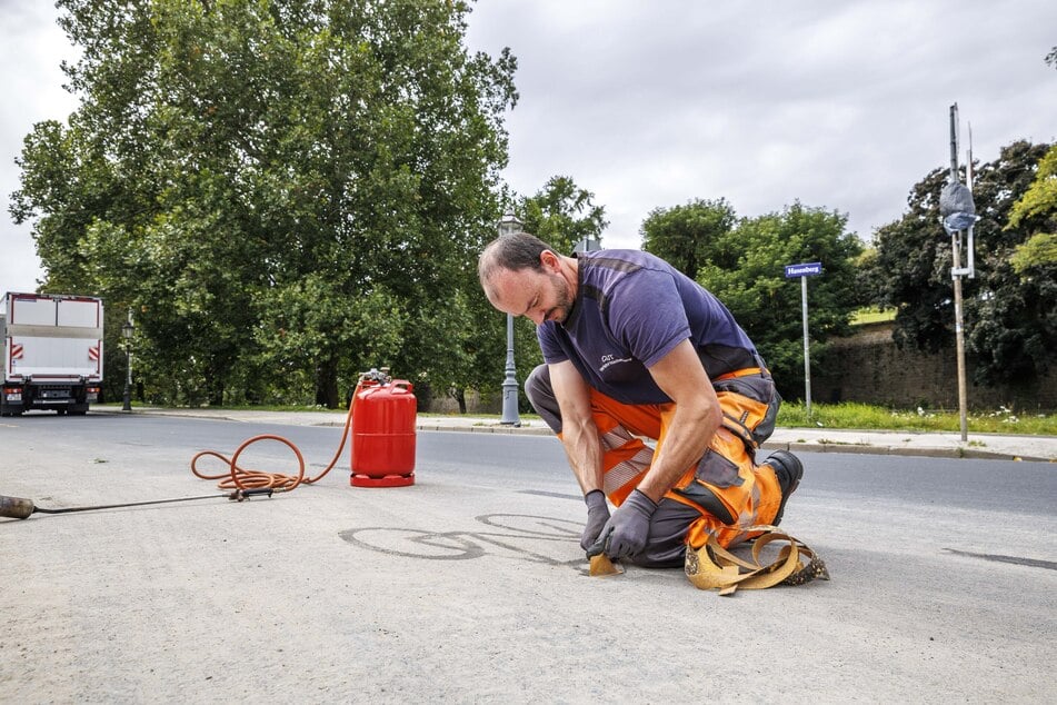 Mitarbeiter kratzen die Markierungen für die Radler-Umleitung von der Straße am Hasenberg.