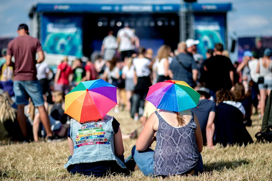 Zwei junge Frauen mit bunten Schirmen auf dem Kopf hören auf dem Hurricane Festival einem Konzert zu.