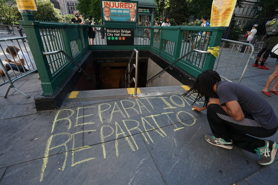 An activist writes "Reparations" on the sidewalk in chalk during 2020 Black Lives Matter protests in New York City.