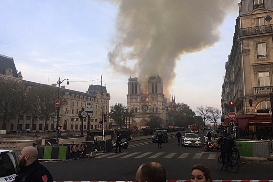 Eine Straße ist abgesperrt, während im Hintergrund Rauch von der Kathedrale Notre-Dame aufsteigt.