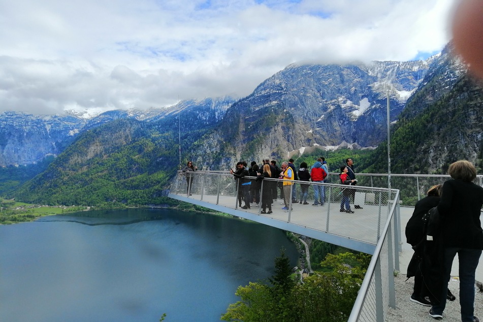 Touristen stehen auf einer Aussichtsplattform über dem Hallstätter See.