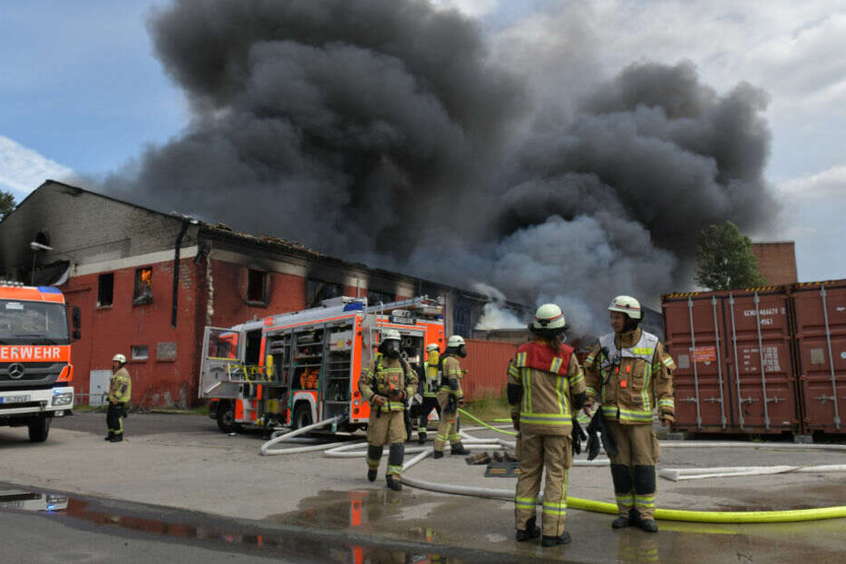Feuerwehrleute stehen vor der Lagerhalle.