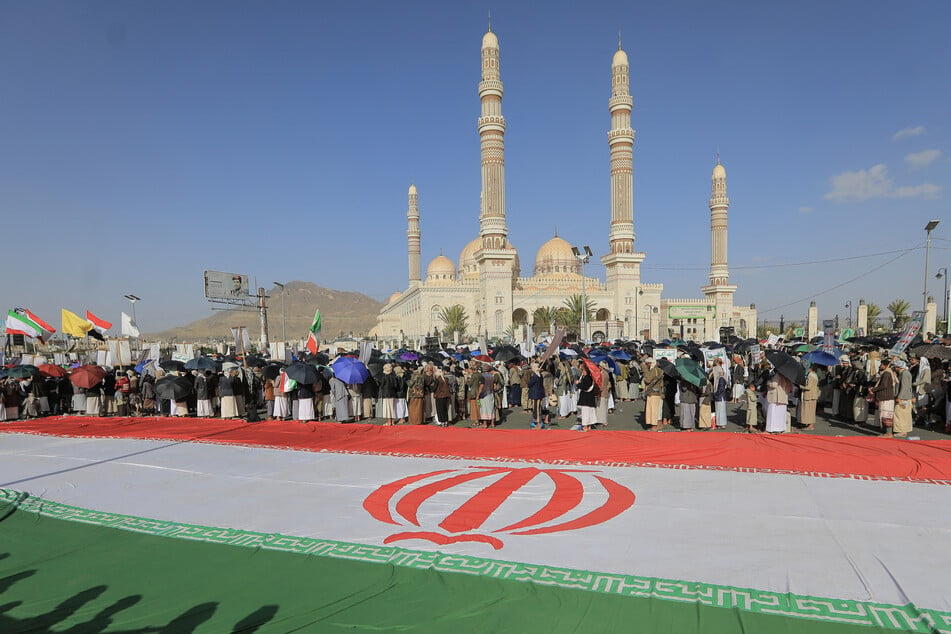Supporters of the Houthi movement stand next to a giant Iranian flag as they rally in solidarity with Iran and Lebanon amid the US-Israeli war, in Sanaa, Yemen, on April 3, 2026.