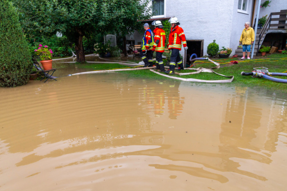 Mitglieder der Feuerwehr pumpen Wasser aus einem Garten ab nach starken Regenfällen in Oberbayern.