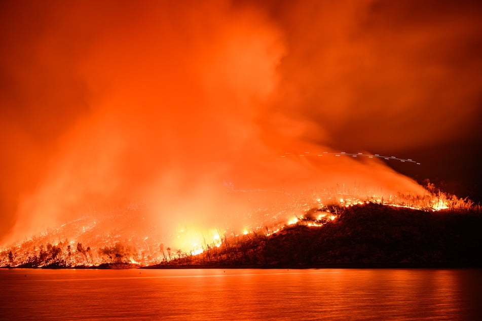 In this long-exposure photograph, a helicopter surveys the scene as the Thompson fire burns around Lake Oroville in Oroville, California on Tuesday.