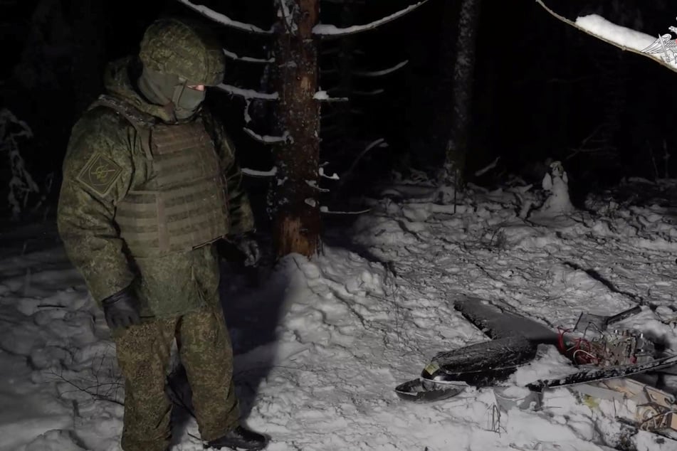 A Russian service member stands next to the remains of a drone, which, according to the Russian Defense Ministry, was downed during the repelling of an alleged Ukrainian attack on the Russian presidential residence in the Novgorod Region.